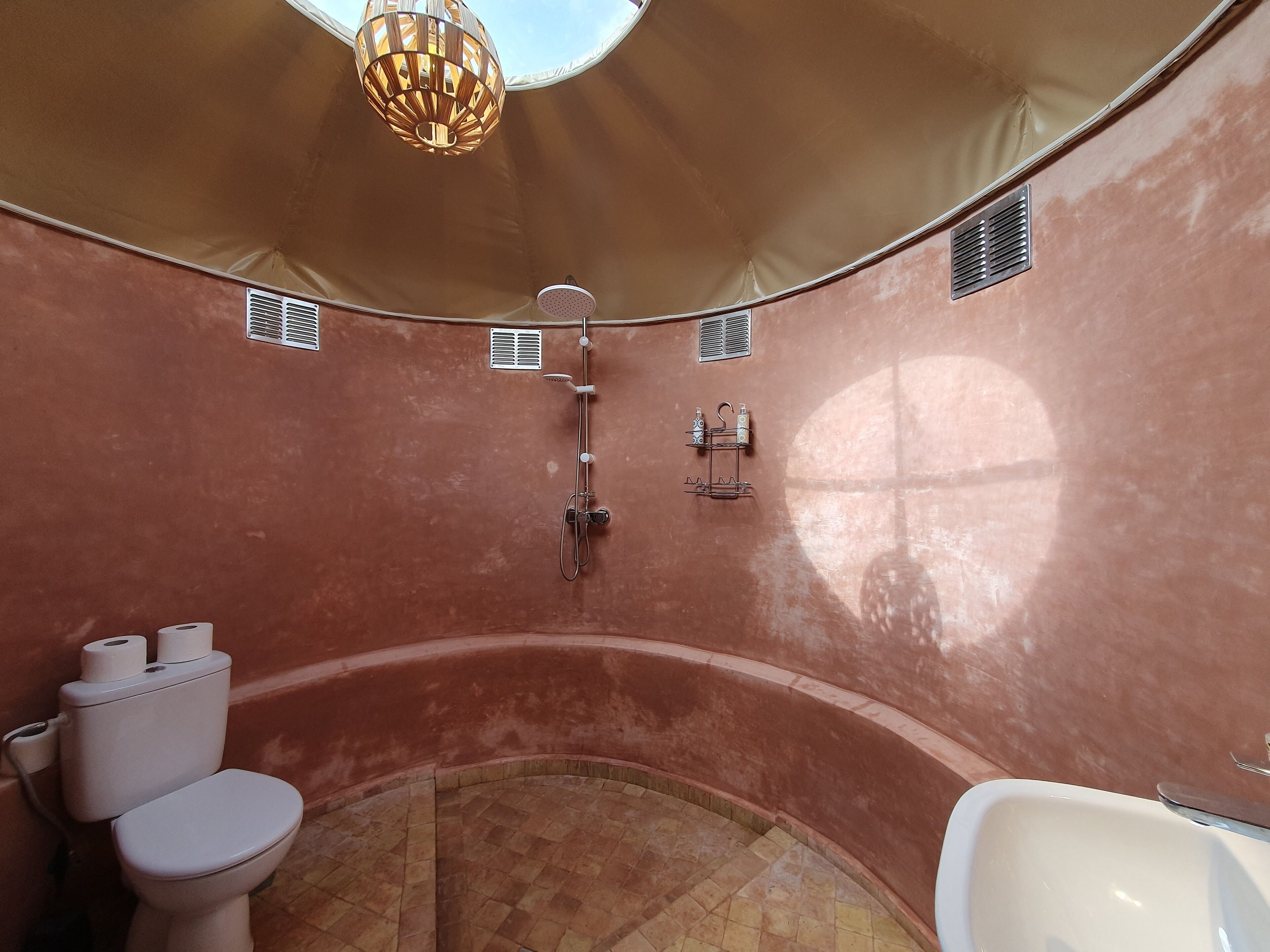 A compact bathroom with a toilet, shower, and sink, featuring a curved design and a ceiling light fixture.