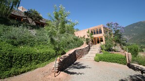 A building with a stone staircase leading to a door, surrounded by greenery and a clear sky. - Kasbah Africa (Ouirgane)