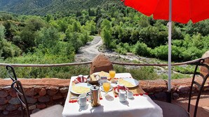 A table set with breakfast items, a red umbrella, and a scenic mountain view. - Kasbah Africa (Ouirgane)