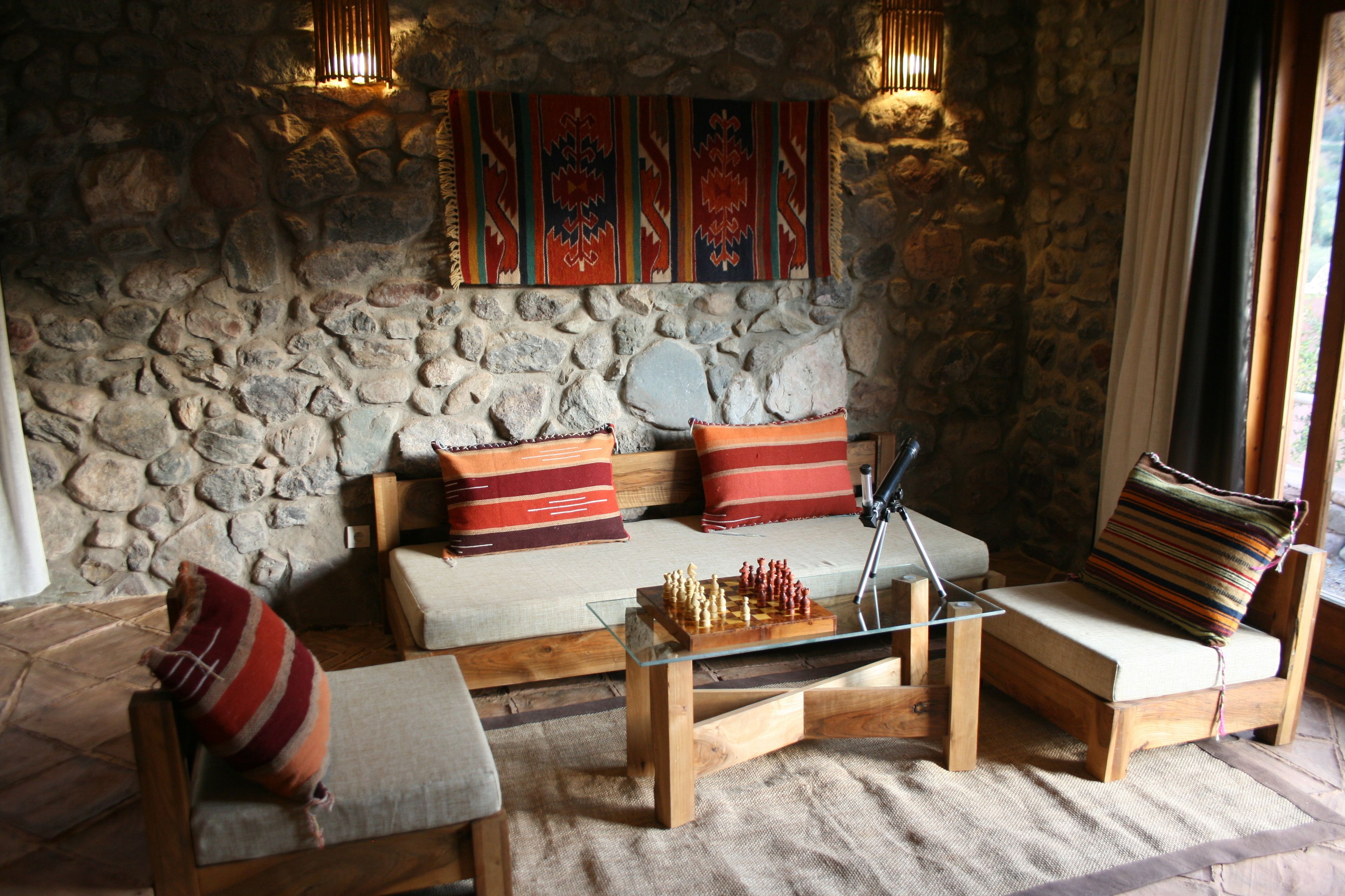 A cozy room with a stone wall, a sofa, a wooden coffee table with chess, and a patterned throw pillow.