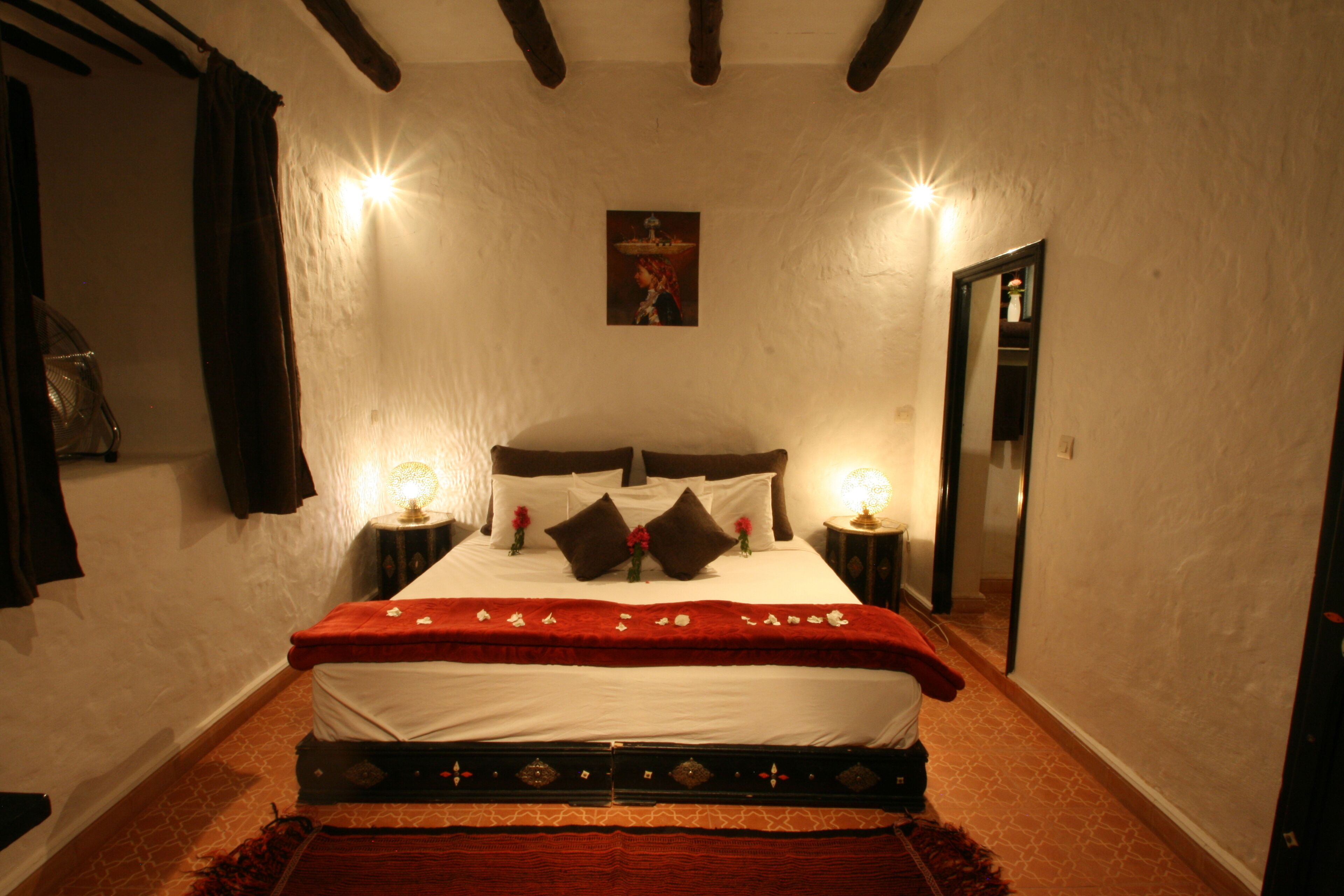 A neatly made bed with a red blanket and pillows, two bedside lamps, and a framed picture on the wall.