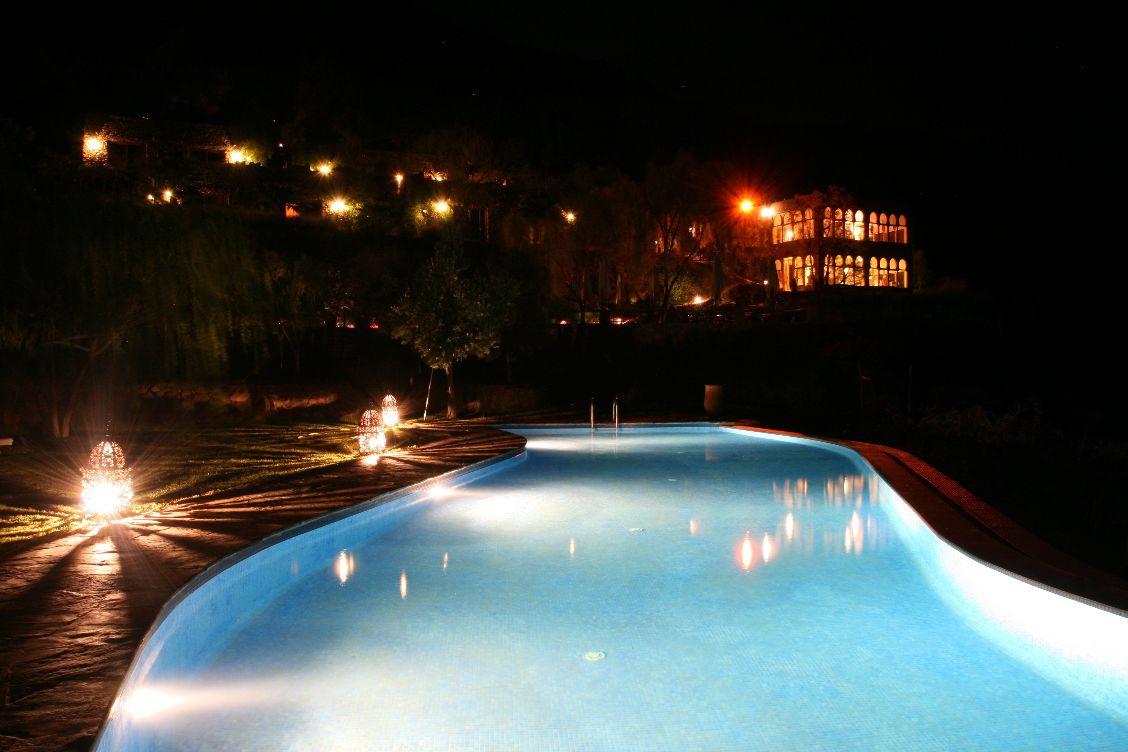 En swimmingpool om natten med omgivende lys og en bygning i baggrunden.