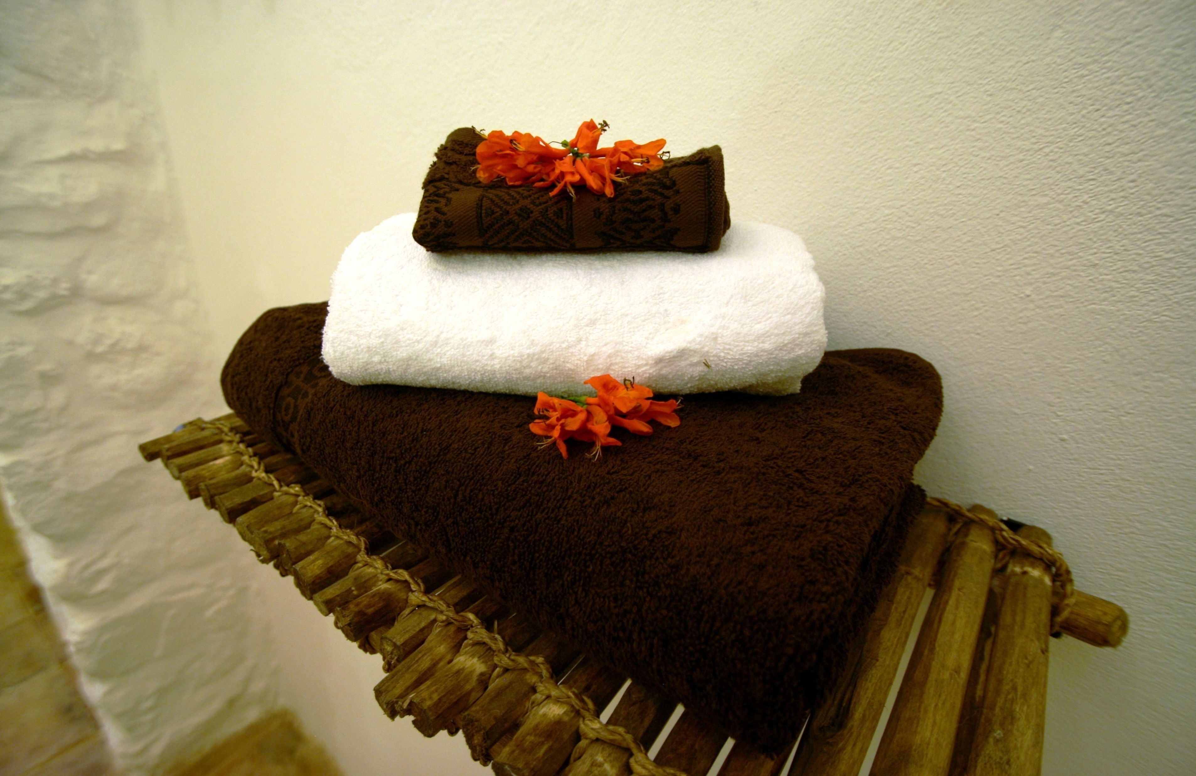 A stack of towels with a decorative flower on top, placed on a wooden chair.