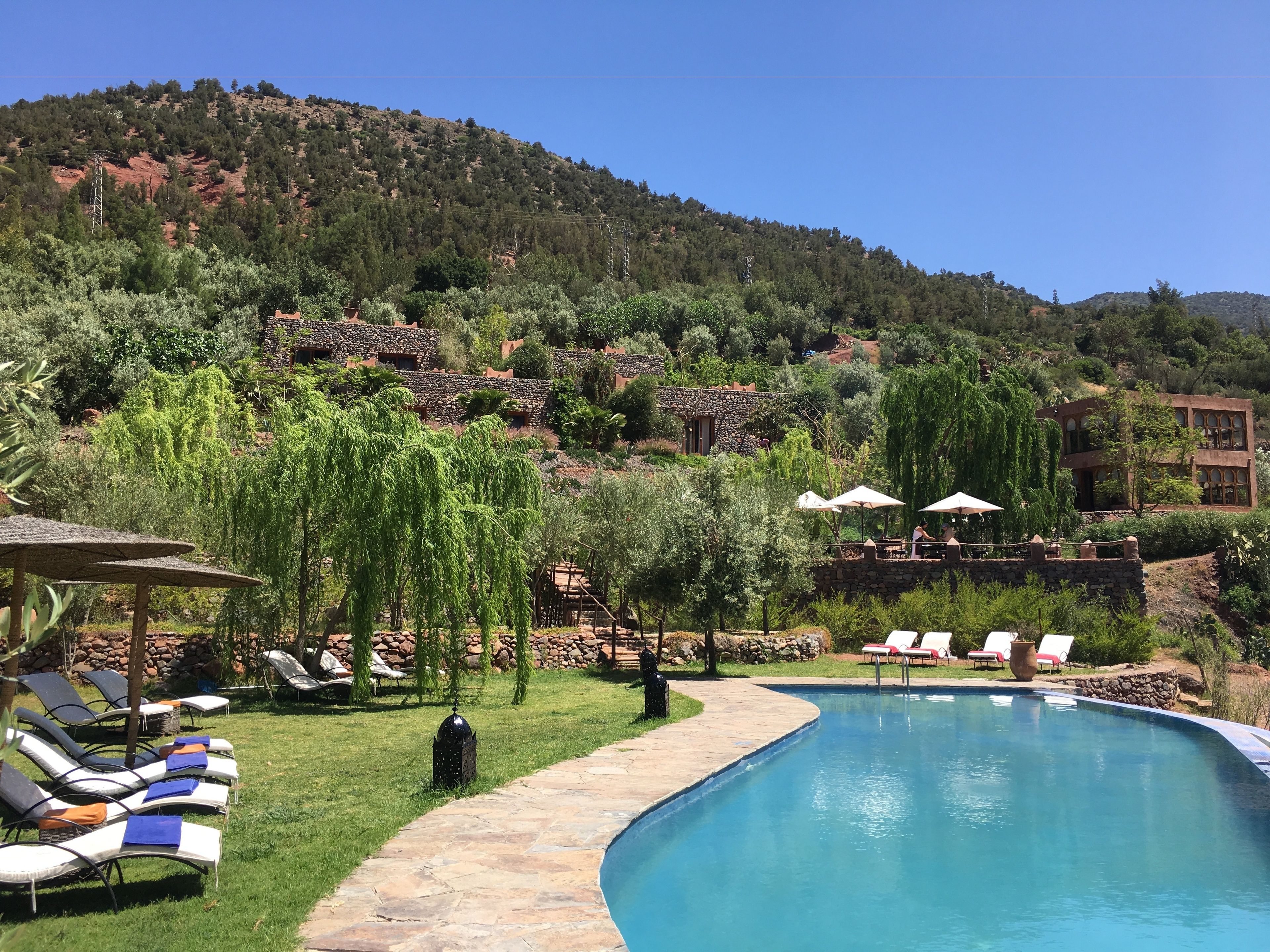 A pool area with lounge chairs, a stone pathway, and a view of a hillside with buildings.
