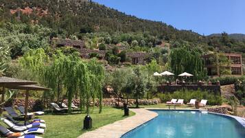 A pool area with lounge chairs, a stone pathway, and a view of a hillside with buildings.
