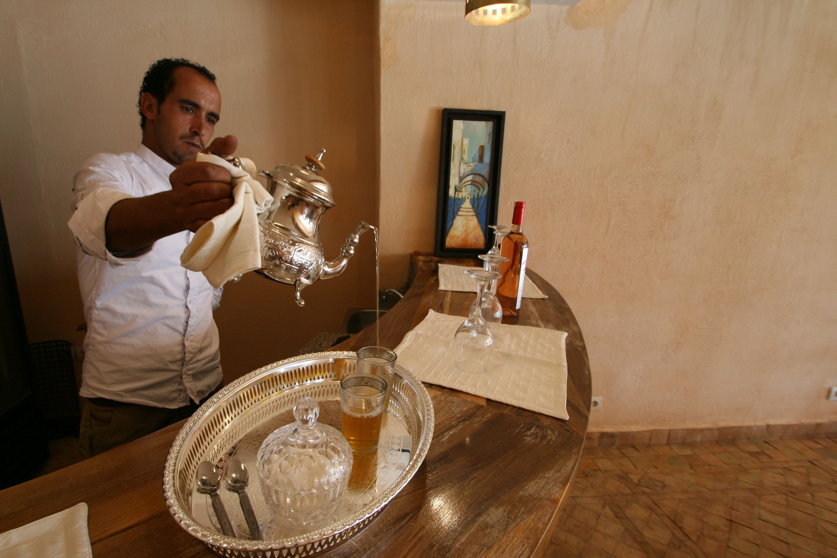 Une personne verse une boisson d’une théière en argent dans un verre posé sur un plateau.