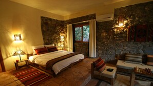A bedroom with a stone wall, a bed with a red and white bedspread, a wooden bench, a small table with chess pieces, and a window with curtains. - Kasbah Africa (Ouirgane)