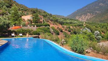 Piscina con vistas a una villa en la ladera y follaje circundante.