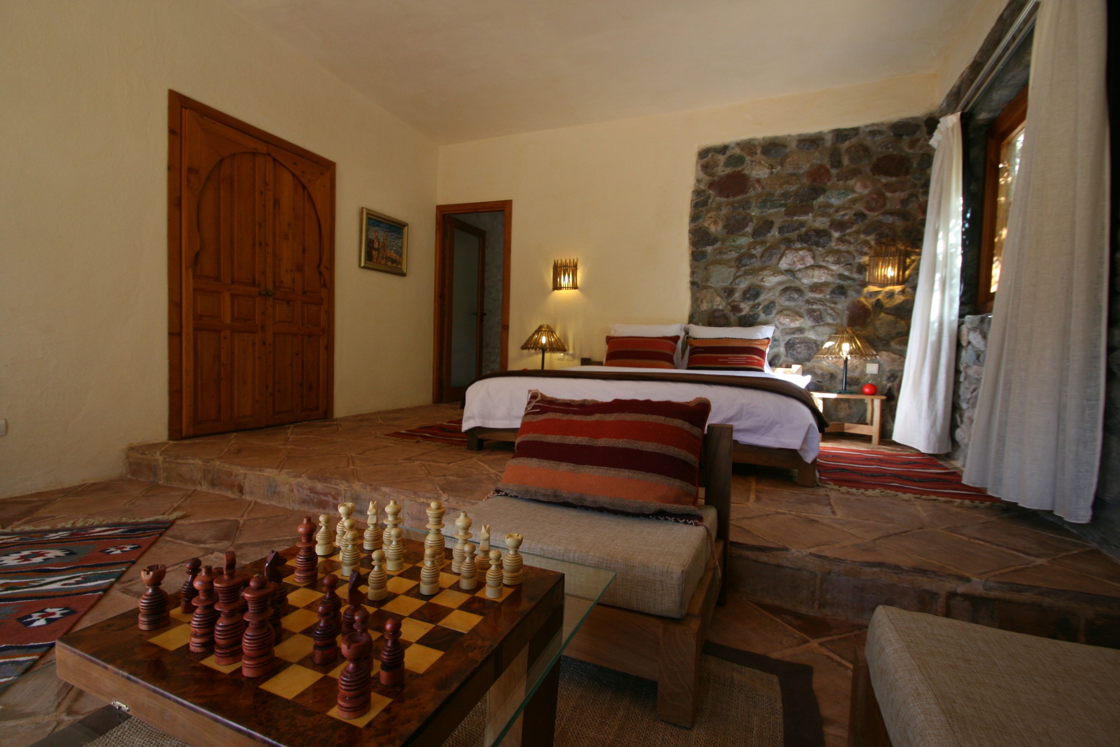 A room with a chessboard, a bed, a stone wall, and a wooden door.