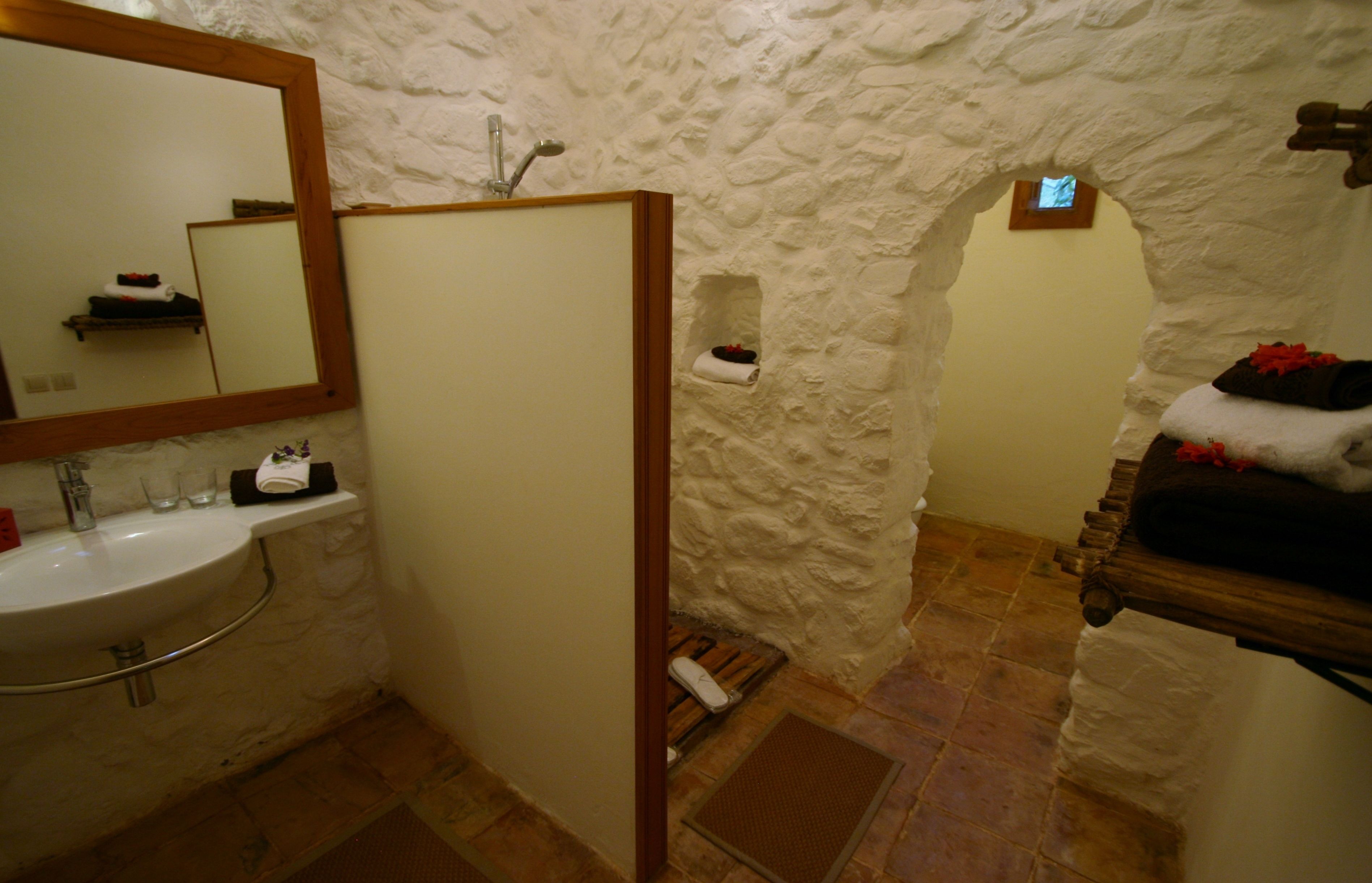 A bathroom with a stone wall, a wooden bench, a sink, and a mirror.