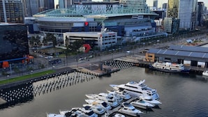 A marina with multiple boats docked, a city skyline in the background, and a modern building with a curved glass facade. - Apartments Melbourne Domain - New Quay Docklands (Docklands)