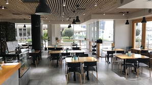 A modern cafe with wooden tables and chairs, large windows, and a sign indicating menu items. - Apartments Melbourne Domain - New Quay Docklands (Docklands)