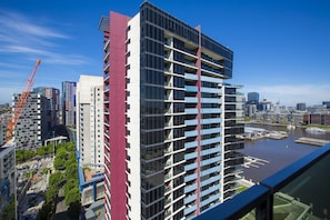 A modern high-rise building with multiple balconies, a river view, and a construction crane in the background.