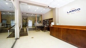 A hotel reception area with a wooden reception desk, a bookshelf, and a staircase leading to an elevator. - Suites Larco 656 (Lima)