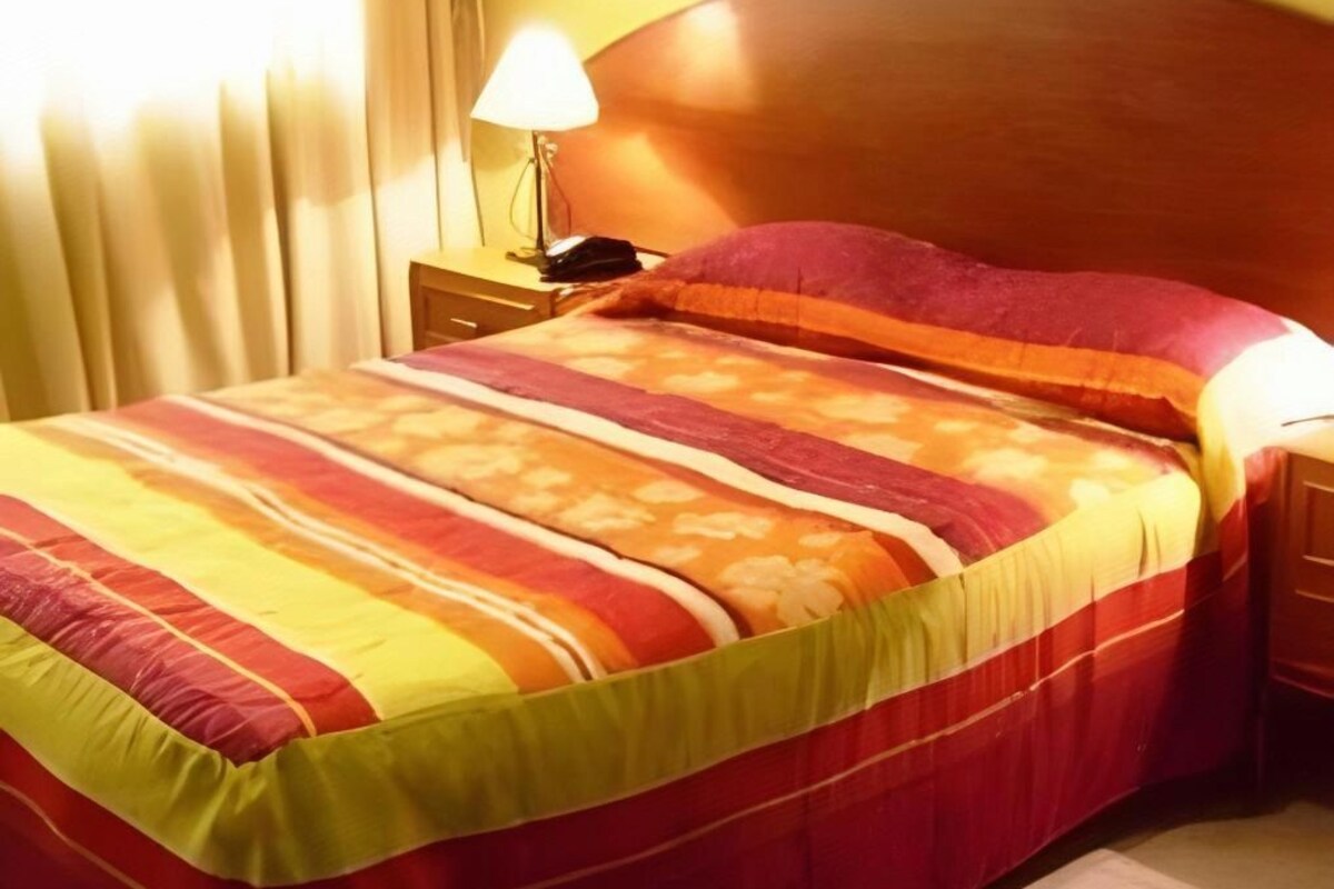 A bed with a striped bedspread, a wooden headboard, a bedside lamp, and a nightstand with a phone.