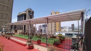 A rooftop terrace with outdoor seating, a covered area, and a view of surrounding buildings.