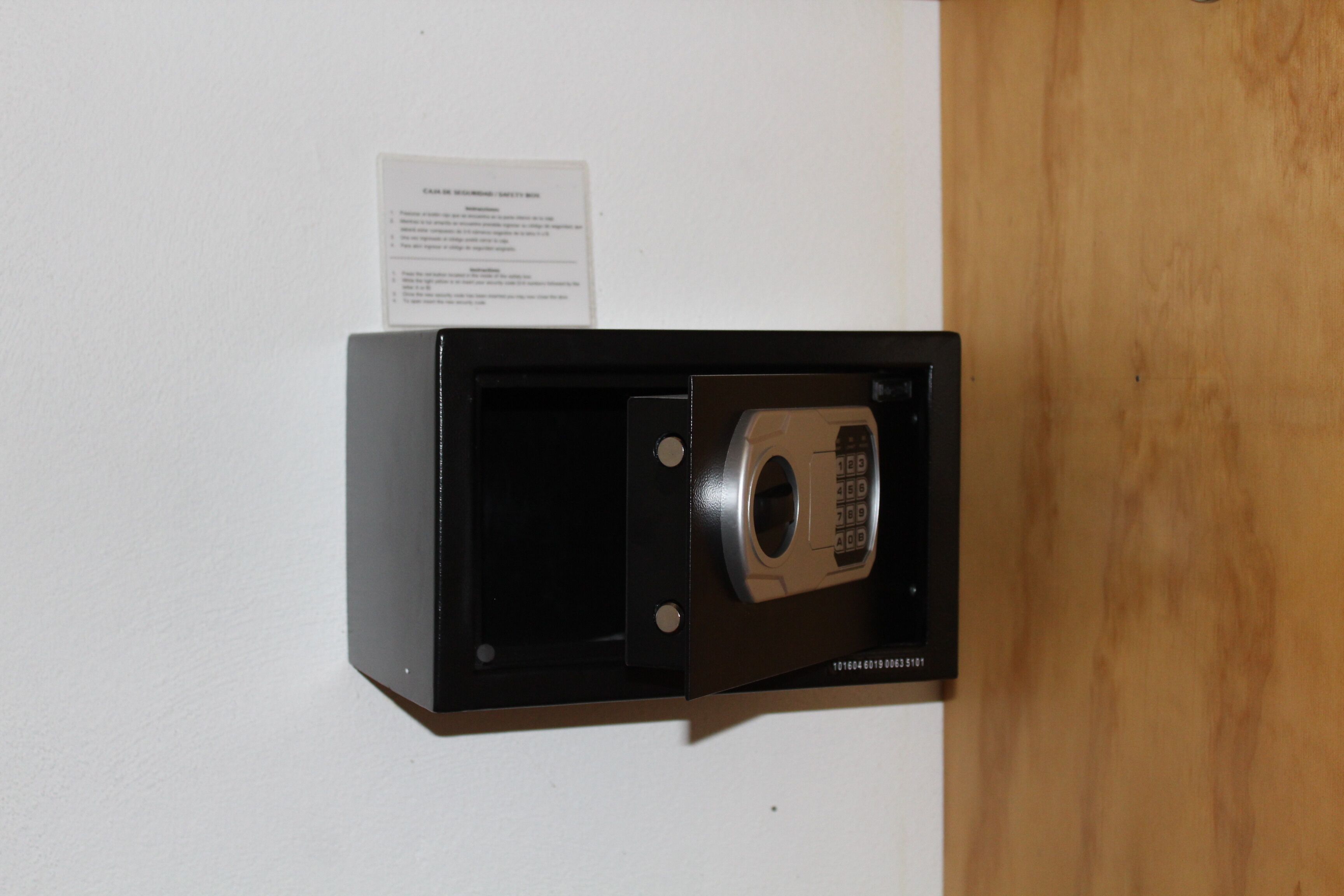 A safe with a keypad, mounted on a wall with a wooden panel.