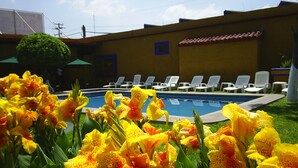 A swimming pool with lounge chairs and yellow flowers in the foreground. - Hotel Hacienda Don Cenobio (San Pablo Villa de Mitla)