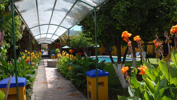 A covered pathway lined with vibrant flowers and a pool area. - Hotel Hacienda Don Cenobio (San Pablo Villa de Mitla)