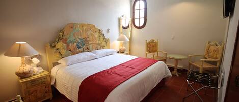 A bedroom with a bed, two chairs, a small table, a decorative headboard, a window, and a ceiling with a painted sky.