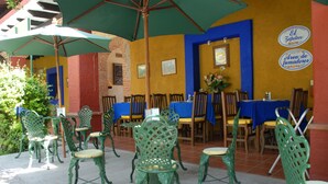 An outdoor patio with green metal chairs and tables, some covered by umbrellas. - Hotel Hacienda Don Cenobio (San Pablo Villa de Mitla)