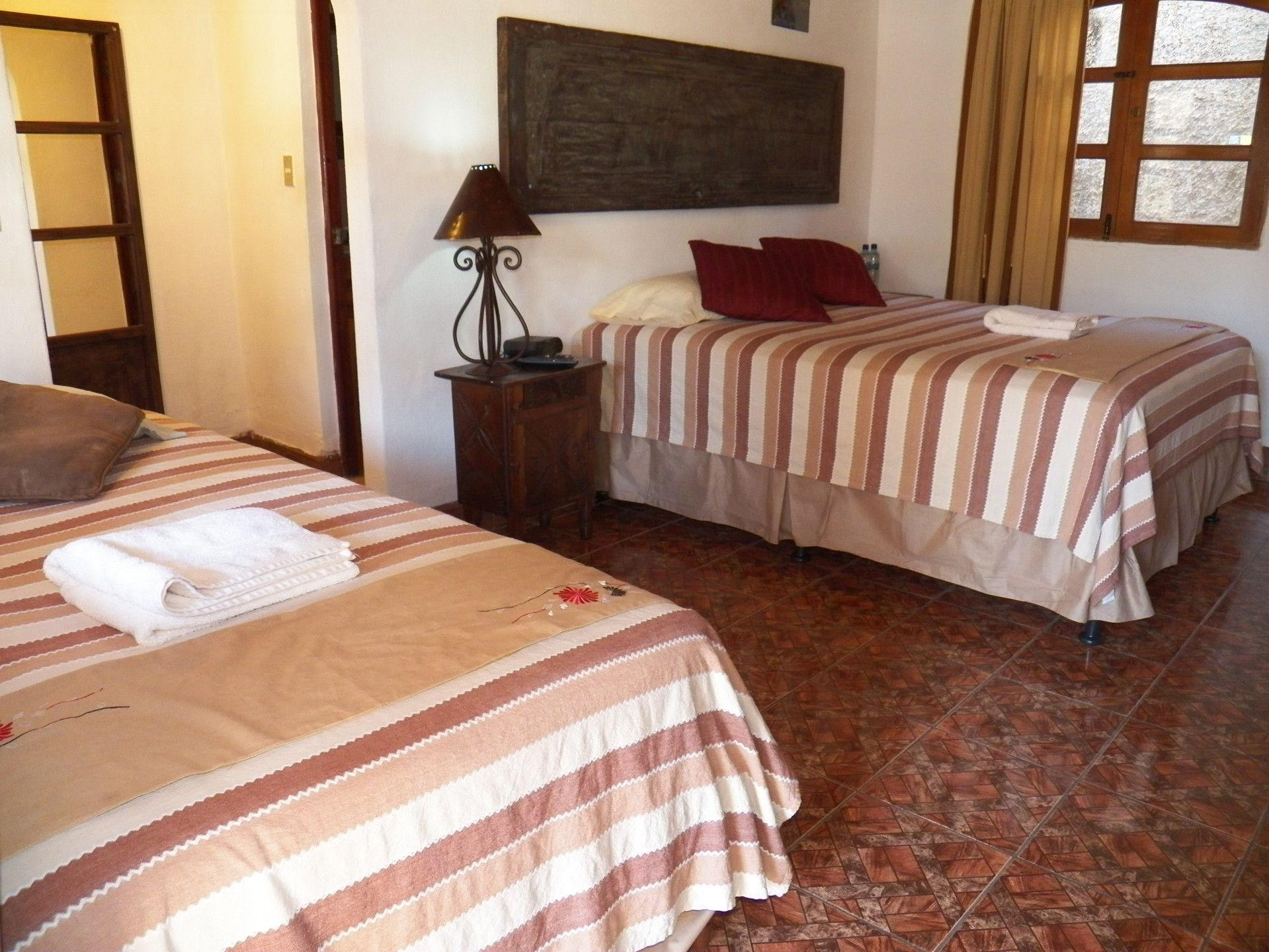 Habitación de hotel con dos camas, una mesita de noche, una lámpara y una ventana con cortinas.