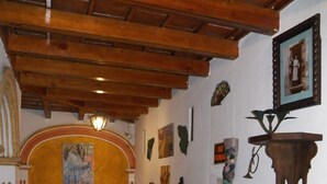 A dining area with wooden tables and chairs, a red drum, and various wall decorations including a framed picture and a sign. - Hotel Ciudad Condal (Antigua Guatemala)