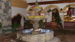 A stone fountain with floral arrangements, surrounded by potted plants and a bench. - Hotel Ciudad Condal (Antigua Guatemala)