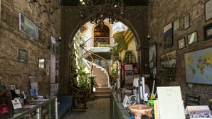 A narrow hallway with stone walls, a staircase leading to an upper level, and a reception desk with informational materials. - Hotel Ciudad Condal (Antigua Guatemala)