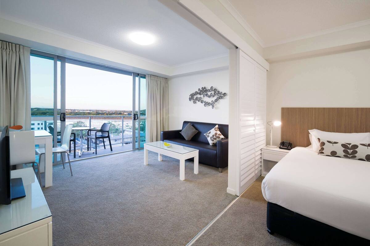 A hotel room with a balcony, a desk, a sofa, a bed, and a nightstand.
