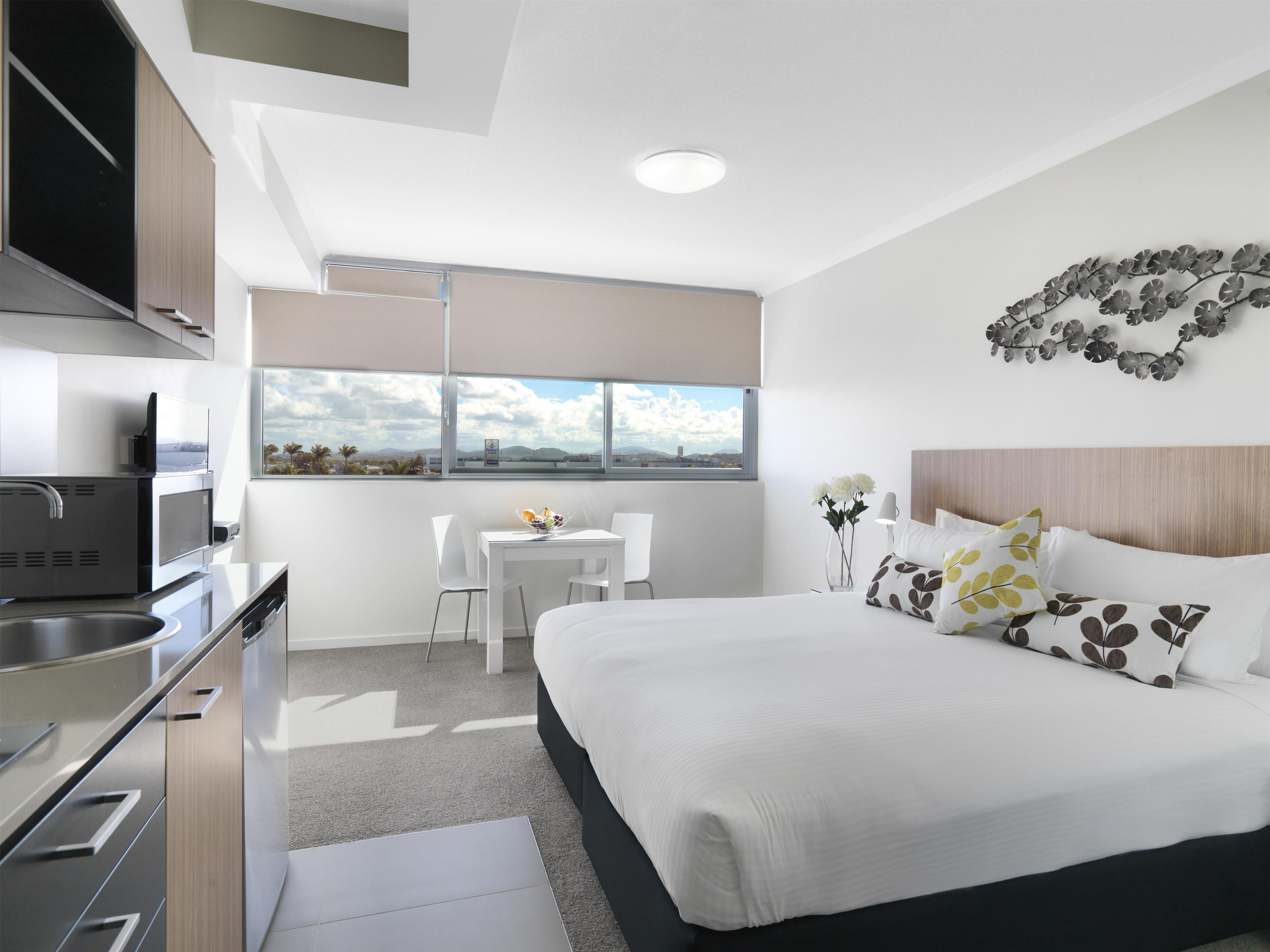 Habitación de hotel moderna con cama, escritorio, silla, zona de cocina y vistas al exterior.