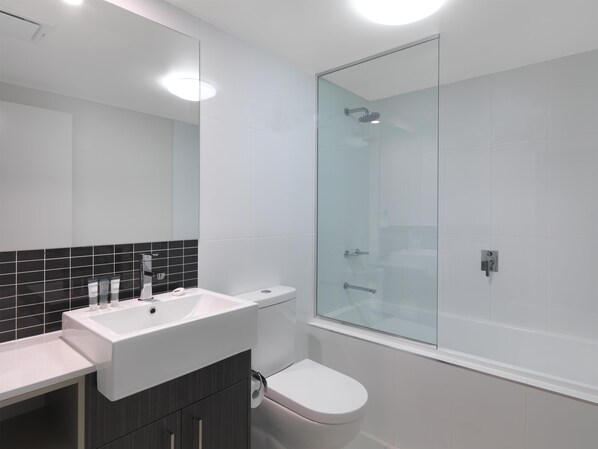 A modern bathroom with a glass shower enclosure, a white sink, and a toilet. - Oaks Mackay Rivermarque Hotel (Mackay)
