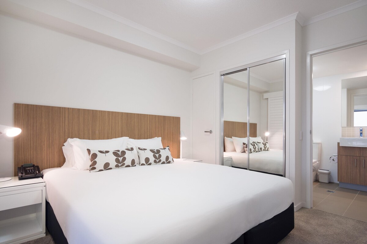 A hotel room with a large bed, bedside tables, a mirror, and a bathroom visible through an open door.