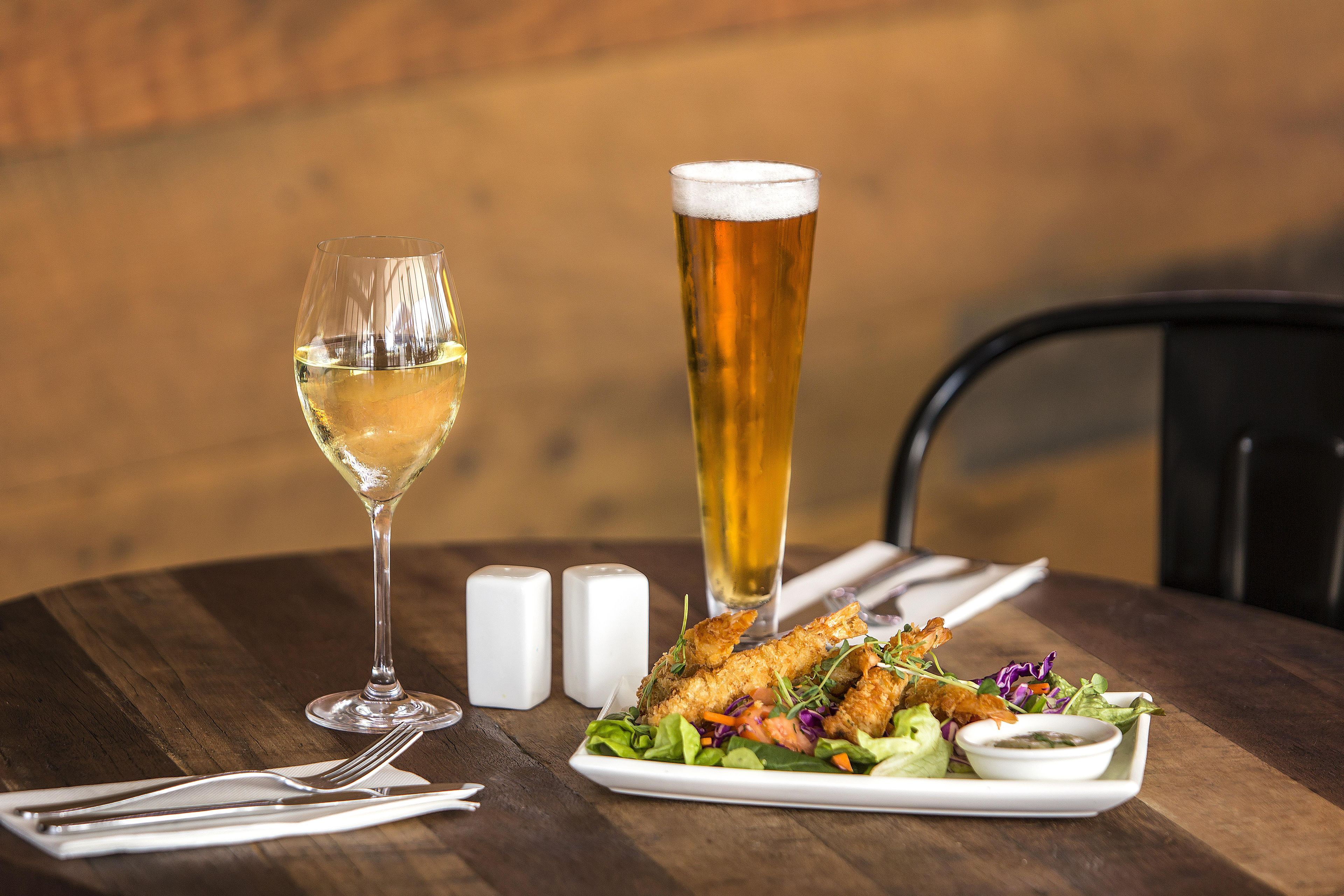 A dining table with a plate of food, a glass of white wine, and a tall glass of beer.