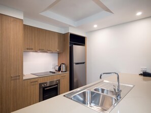 A modern kitchen with wooden cabinets, stainless steel appliances, and a double sink. - Oaks Mackay Rivermarque Hotel (Mackay)