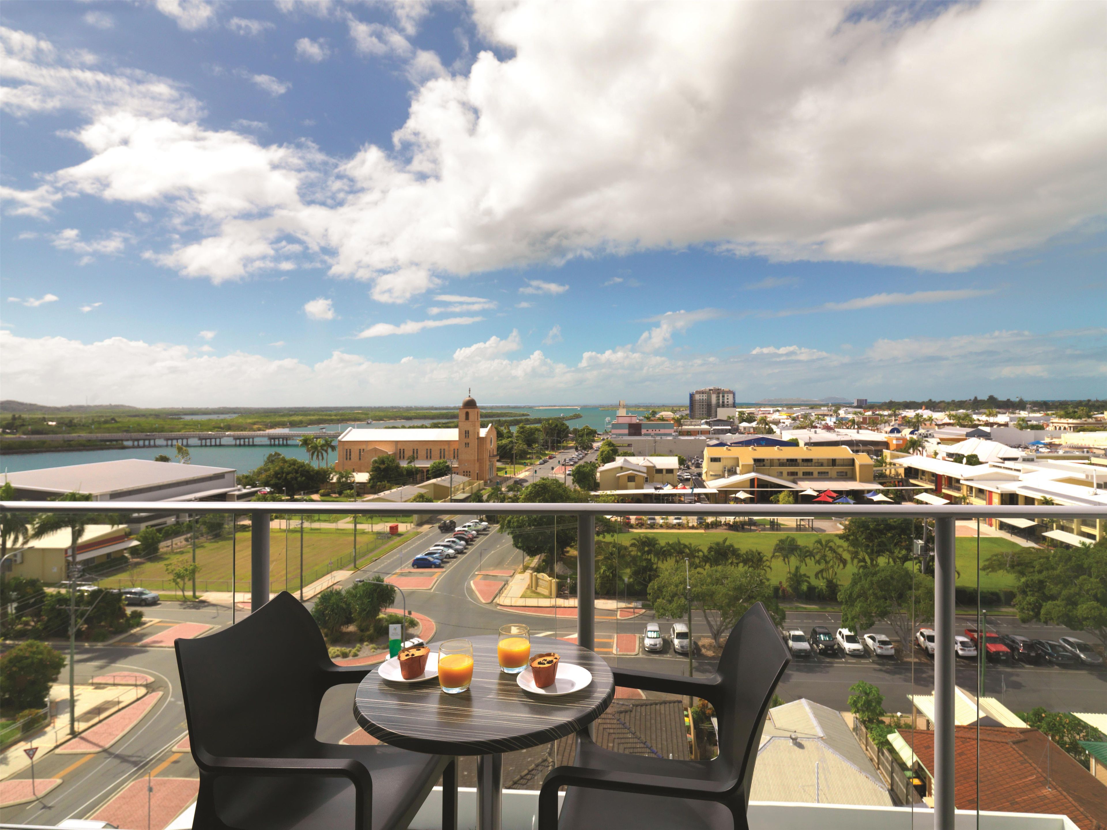 A balcony with a table set for breakfast, overlooking a cityscape with buildings and a body of water.