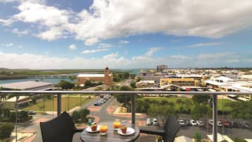 A balcony with a table set for breakfast, overlooking a cityscape with buildings and a body of water.