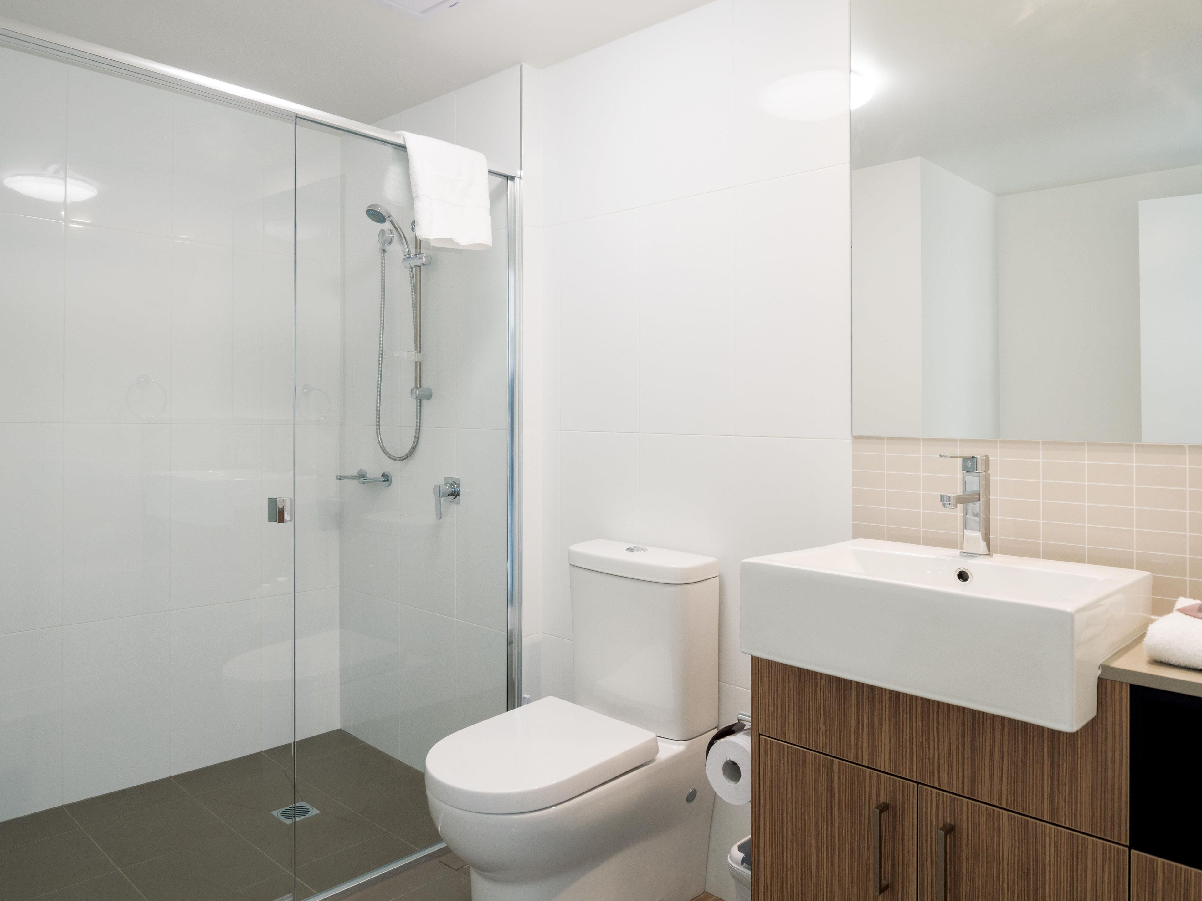 A modern bathroom with a glass shower enclosure, a toilet, a sink, and a mirror.