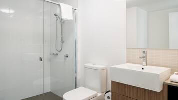 A modern bathroom with a glass shower enclosure, a toilet, a sink, and a mirror.