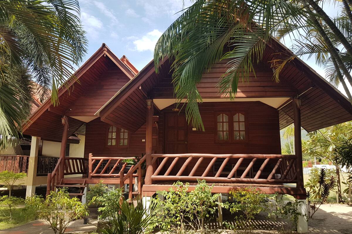 A wooden cabin with a porch, surrounded by tropical vegetation.