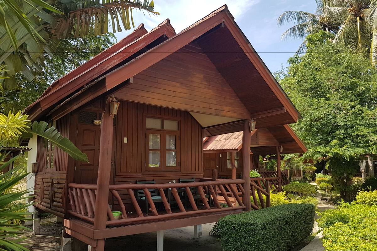 A wooden cabin with a porch, surrounded by lush greenery and palm trees.