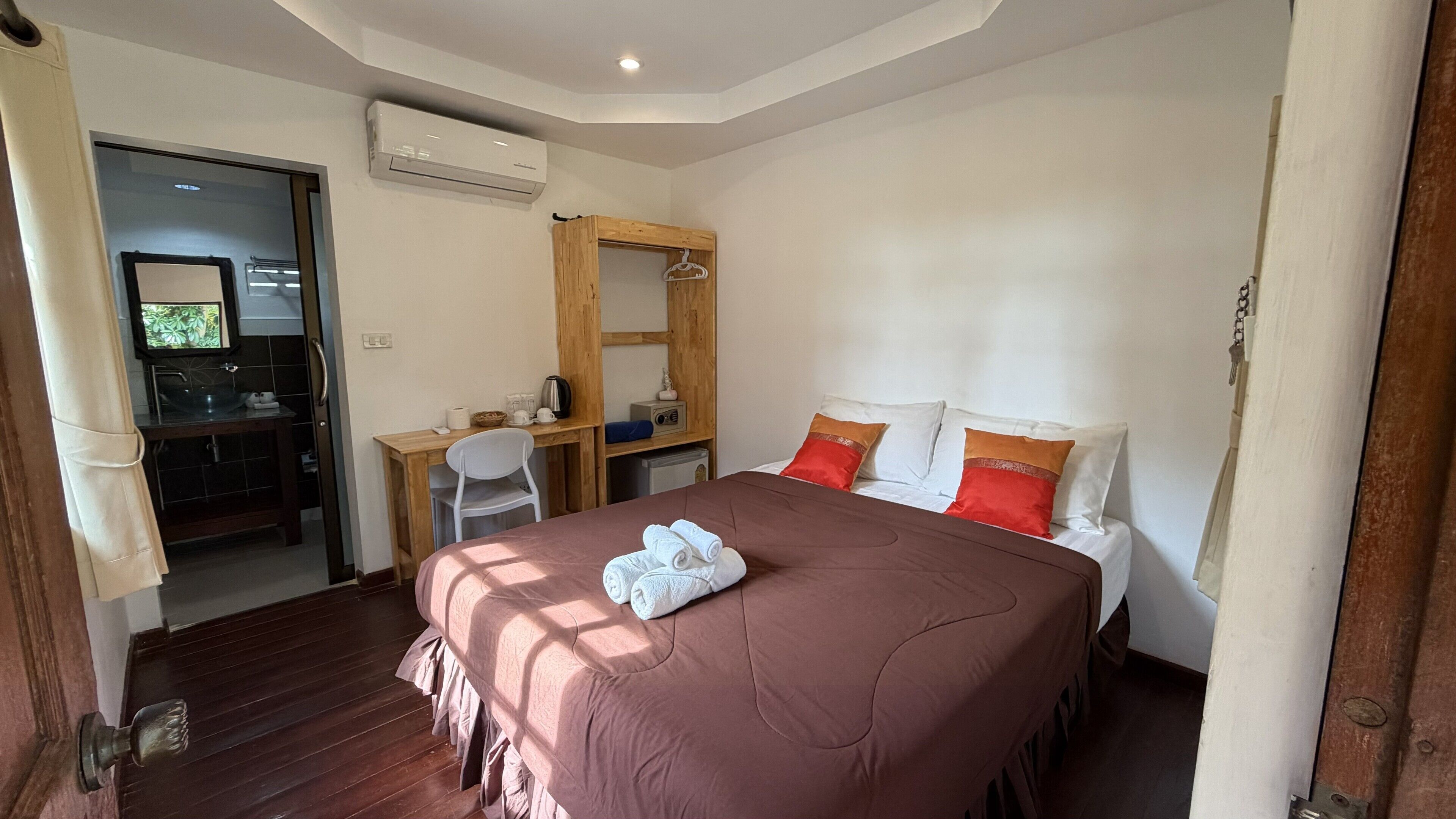 Un dormitorio con cama, escritorio, silla, armario y aire acondicionado.