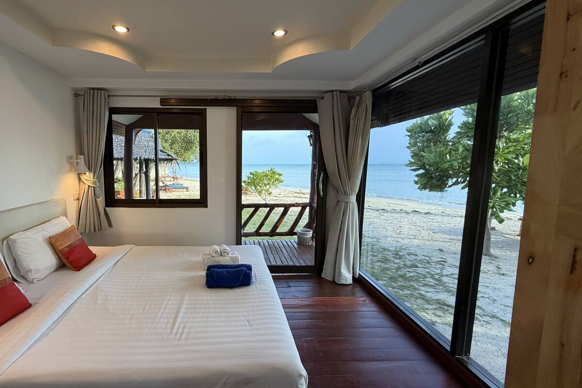 A bedroom with a large bed, a view of the beach, and a balcony with a wooden railing.
