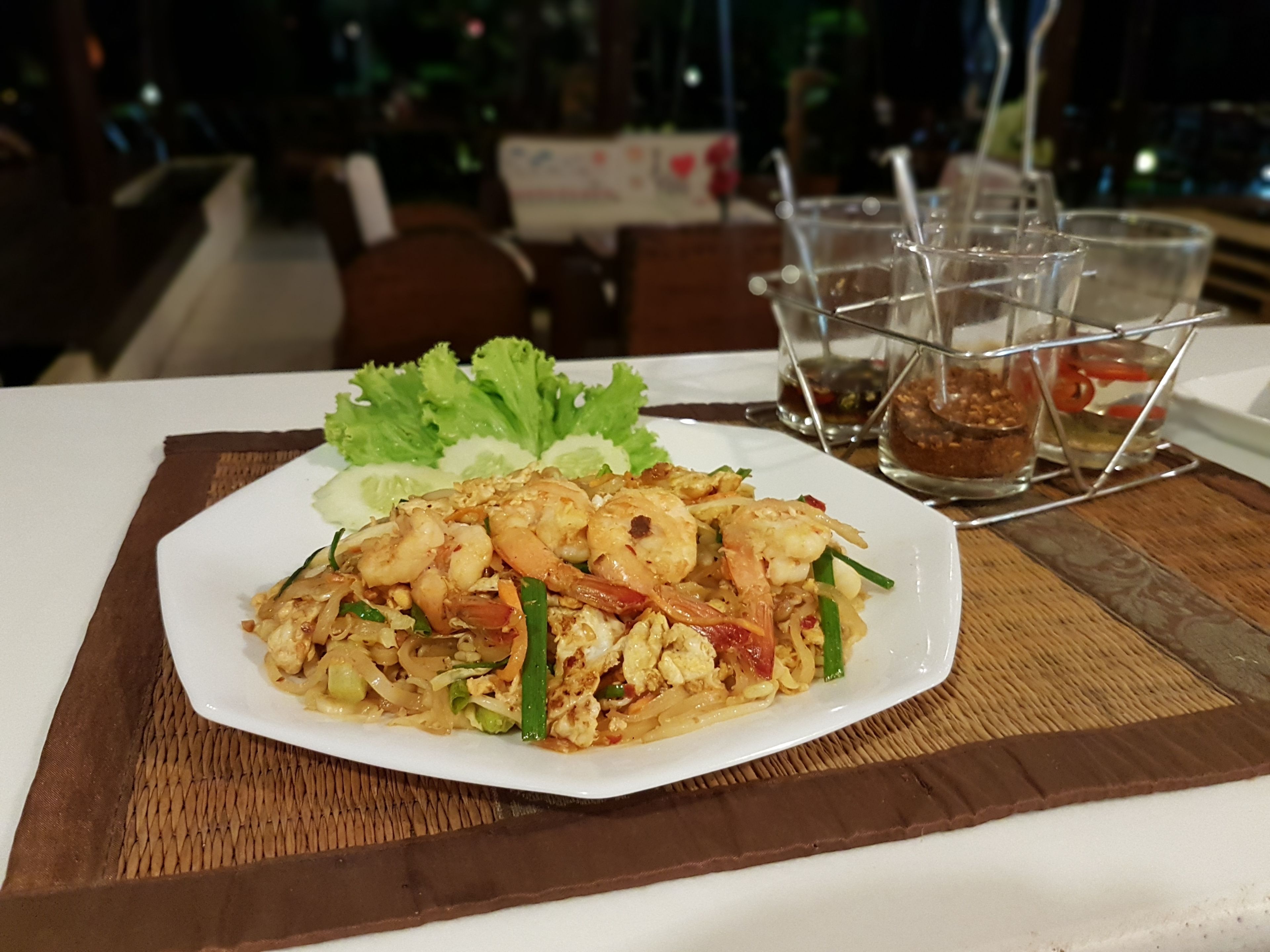 A plate of shrimp and noodle dish with vegetables on a white plate, placed on a wooden placemat.