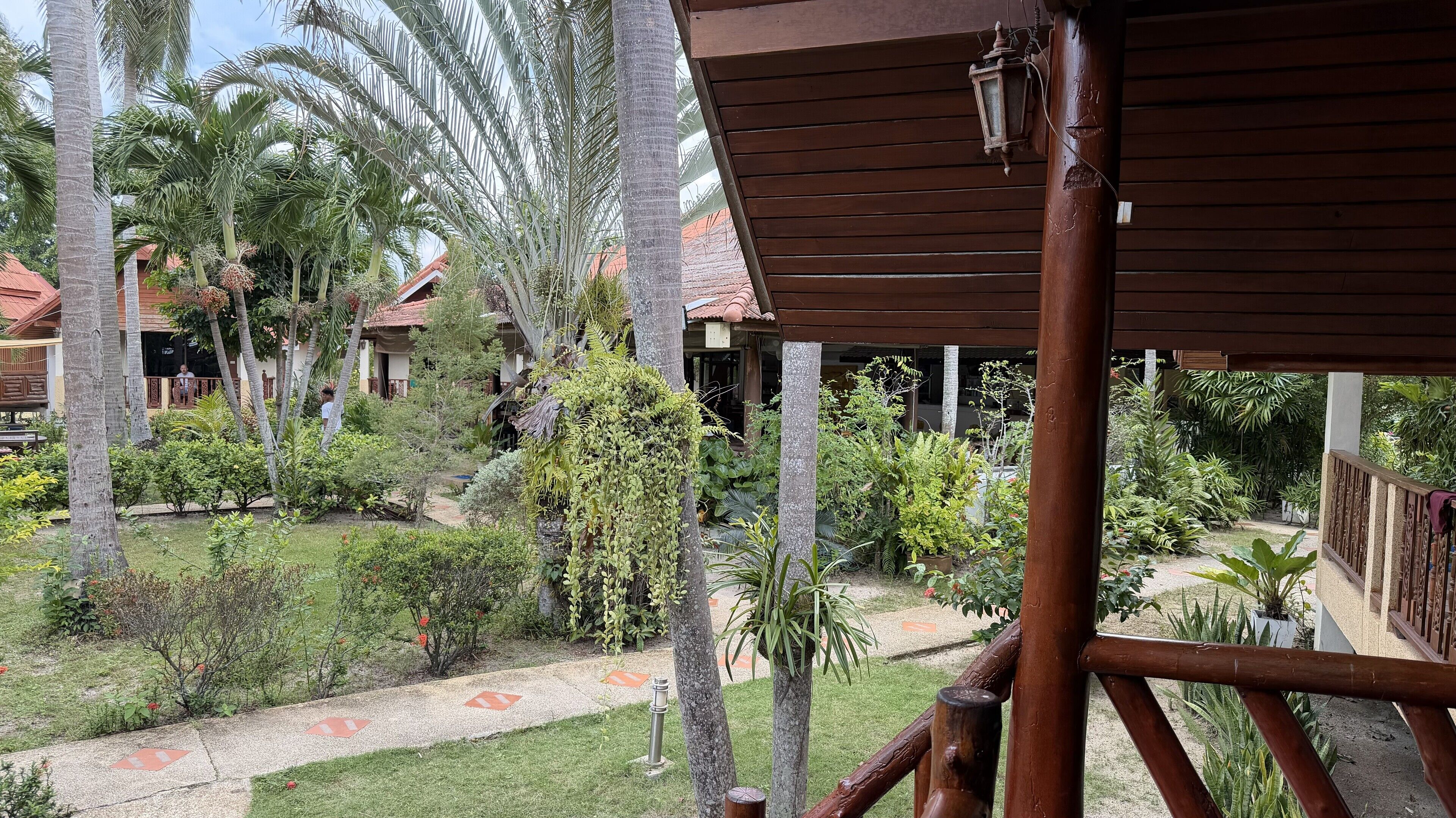 Un jardín tropical con palmeras y diversas plantas, estructuras de madera y un sendero.