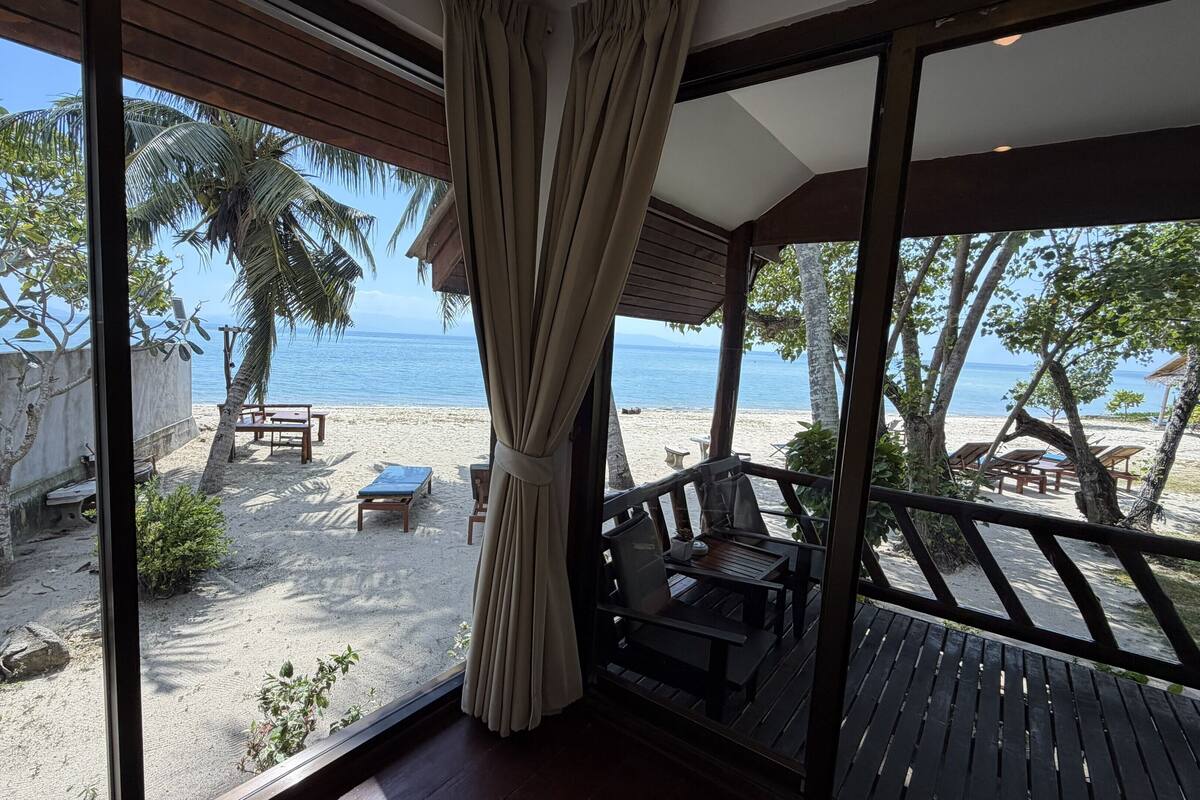 A beach view from a covered deck with a wooden railing, a table, and chairs.