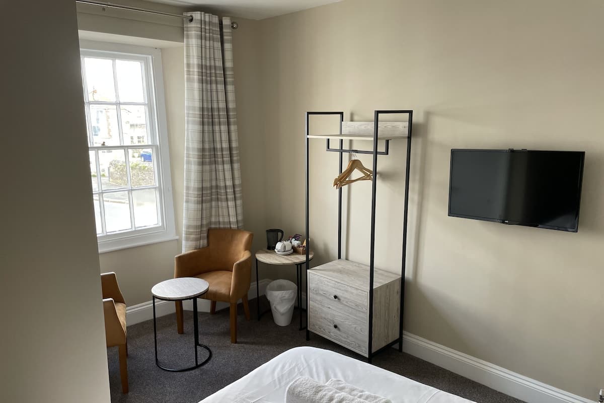 Une chambre d’hôtel avec un lit, une chaise, une petite table, un téléviseur et une fenêtre avec des rideaux.