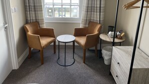 A hotel room with two armchairs, a small round table, a dresser, and a window with curtains.