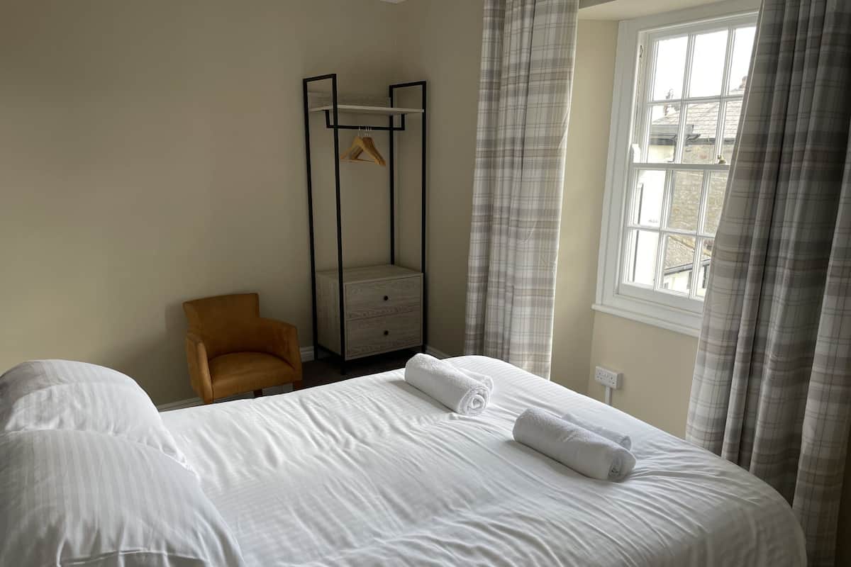 Une chambre d’hôtel avec un grand lit, une chaise en bois, une armoire et une fenêtre avec des rideaux.