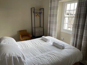 A hotel room with a large bed, a wooden chair, a wardrobe, and a window with curtains. - Duke of Cornwall (St Austell)